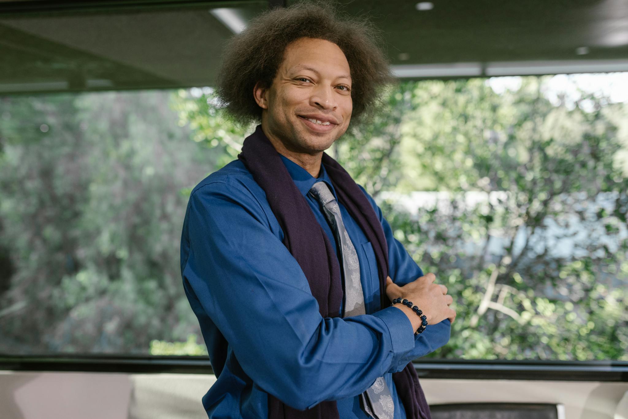 Smiling business professional posing confidently in a modern office with greenery outside.